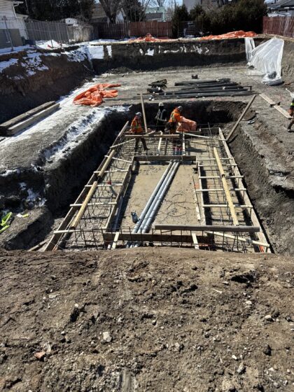 Ouvriers travaillant sur un coffrage de fondation armé avec plomberie souterraine, dans une excavation enneigée