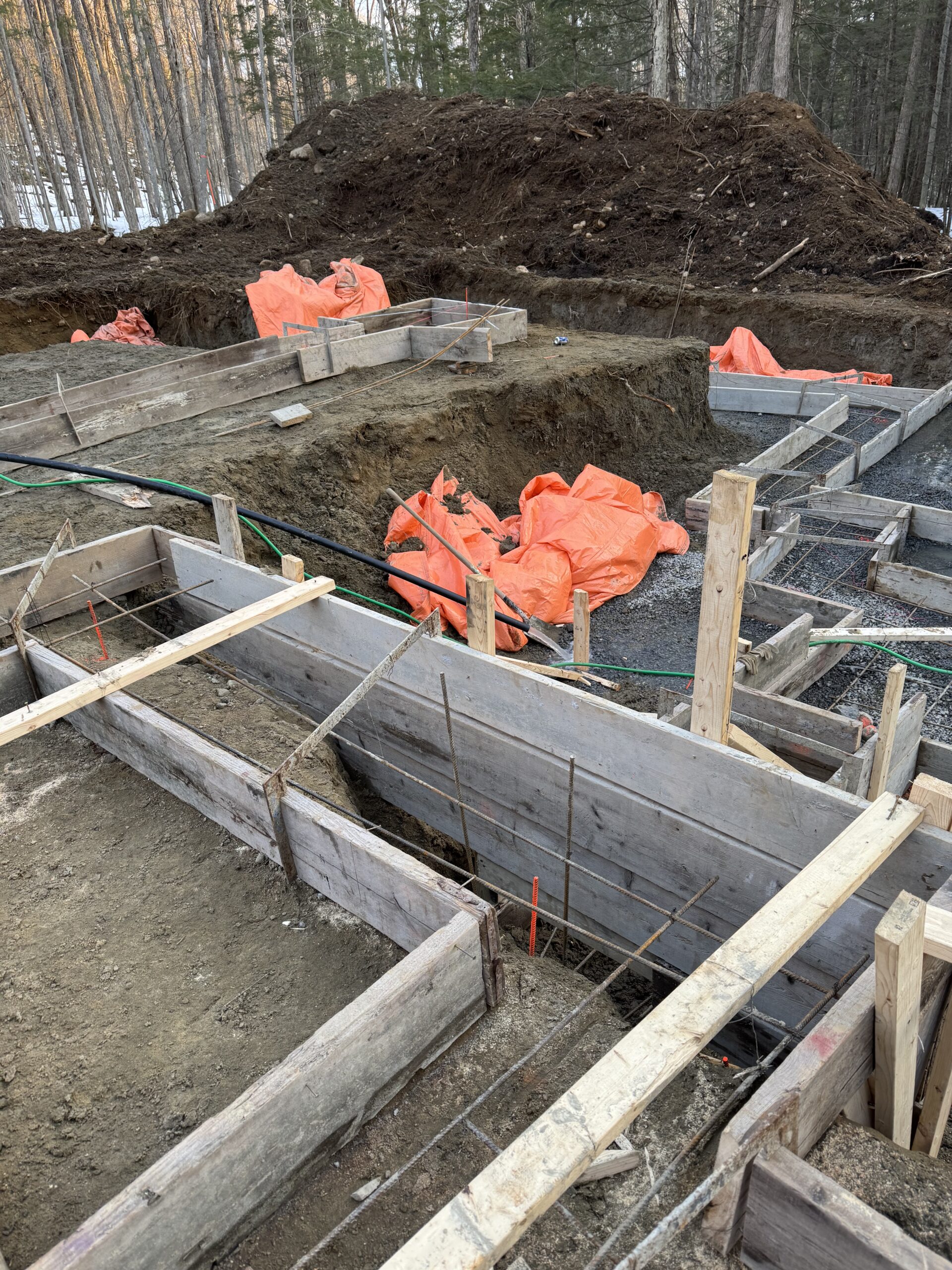 Coffrages de semelles de fondation en bois installés sur un terrain excavé en forêt et protégés par des bâches