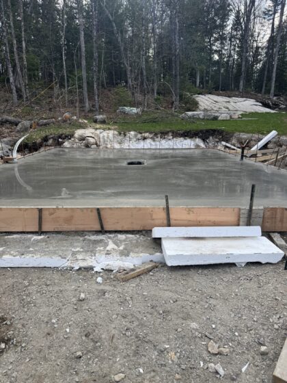 Dalle de béton fraîchement coulée et lissée dans une clairière boisée, coffrage de bois encore en place