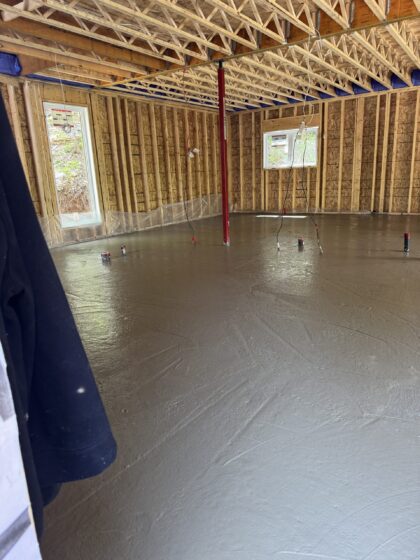 Dalle de béton intérieure fraîchement finie dans un bâtiment charpenté avec fermes de toit apparentes