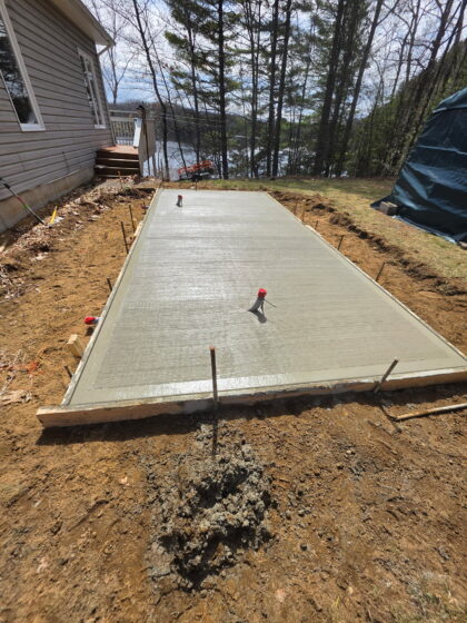 Dalle de béton rectangulaire fraîchement coulée avec finition balai, coffrage de bois encore en place