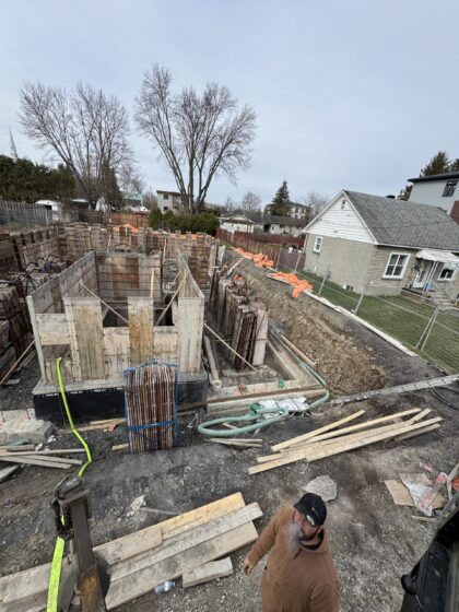 Vue d'ensemble d'un chantier de fondation résidentielle avec coffrages montés et boyau de pompe à béton