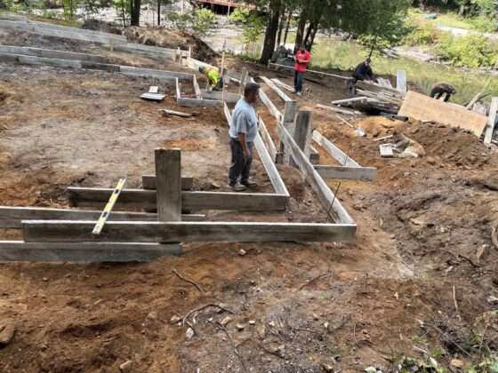Équipe d'ouvriers installant des coffrages de semelles de fondation sur un terrain en pente près d'un cours d'eau