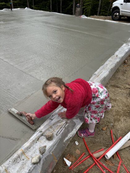 Jeune enfant tenant une truelle sur le bord d'une dalle de béton fraîchement coulée