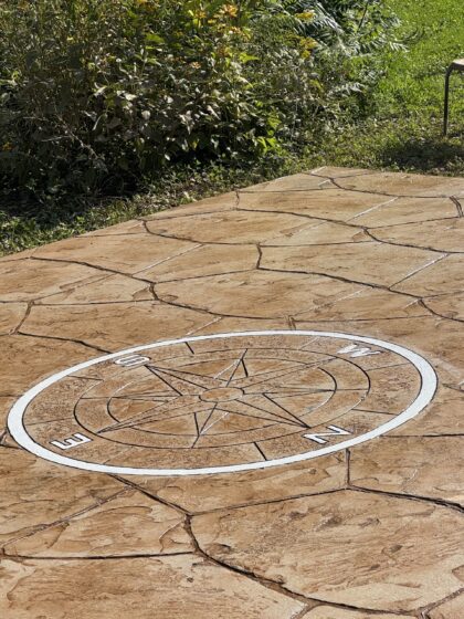 Gros plan d'un médaillon rose des vents blanc gravé dans une surface de béton estampé beige