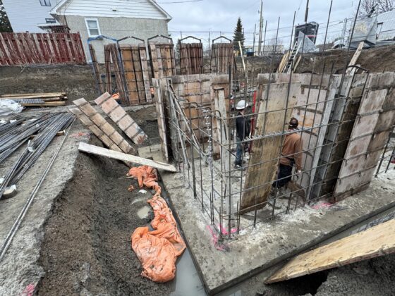 Ouvriers montant des coffrages de murs de fondation avec armature verticale sur une semelle coulée