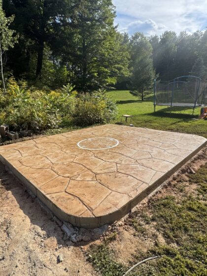 Patio carré en béton estampé beige orné d'un médaillon rose des vents, aménagé dans une cour arrière