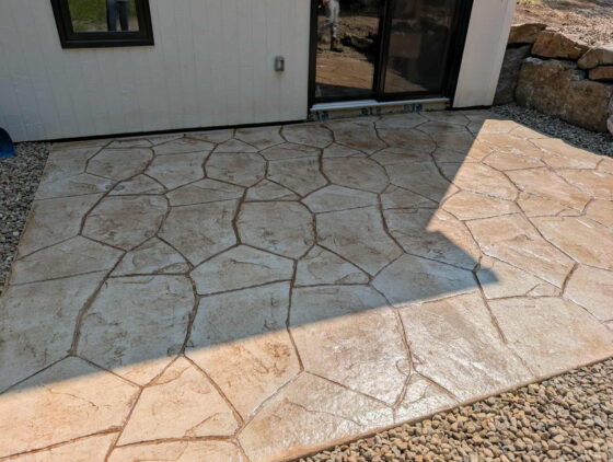 Patio en béton estampé beige imitant la pierre des champs, aménagé devant la porte-patio d'une maison