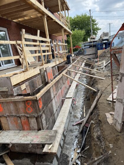 Coffrages de bois installés le long d'un bâtiment de brique étayé pour la réfection de sa fondation