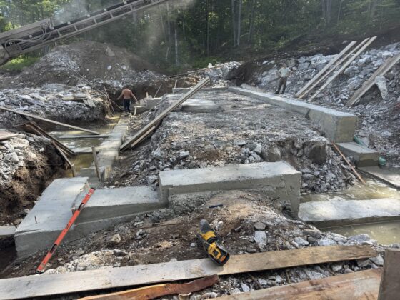Semelles de fondation coulées en gradins dans le roc d'un terrain en forte pente, convoyeur à béton à l'arrière